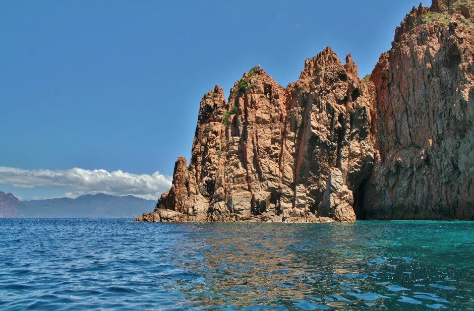 Vue d'une falaise rose plongeant dans la mer en Corse.