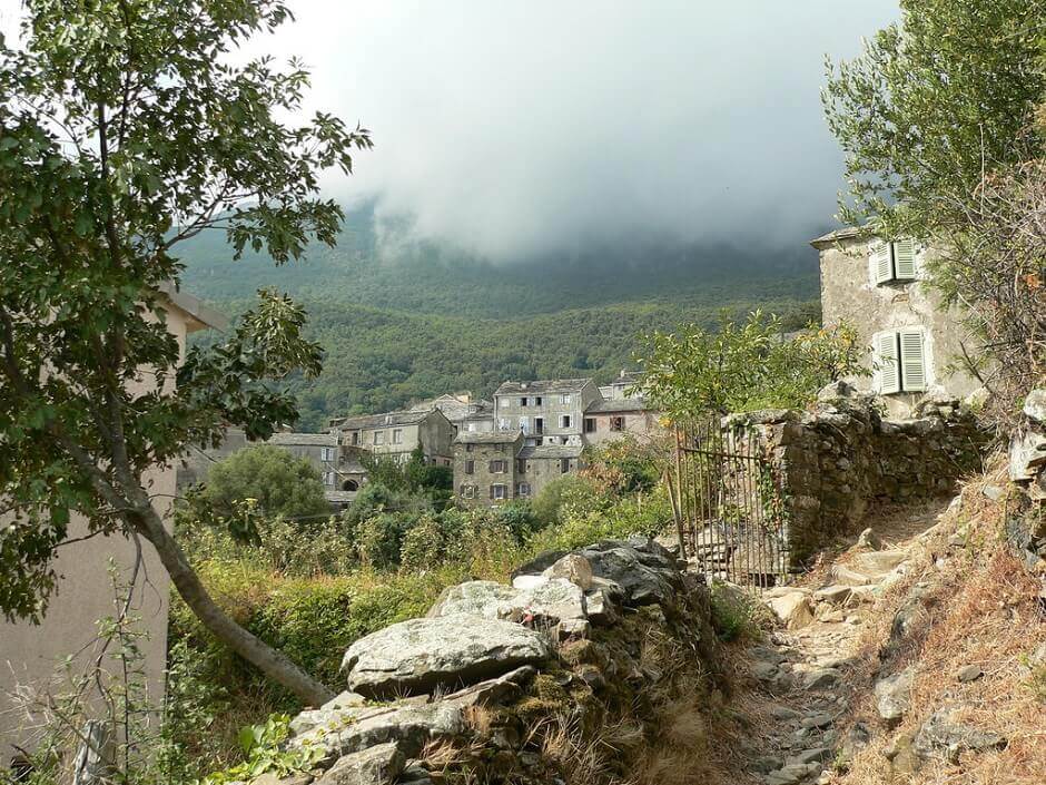 Vue d'un vieux hameau corse dans la montagne, traversé par un sentier.