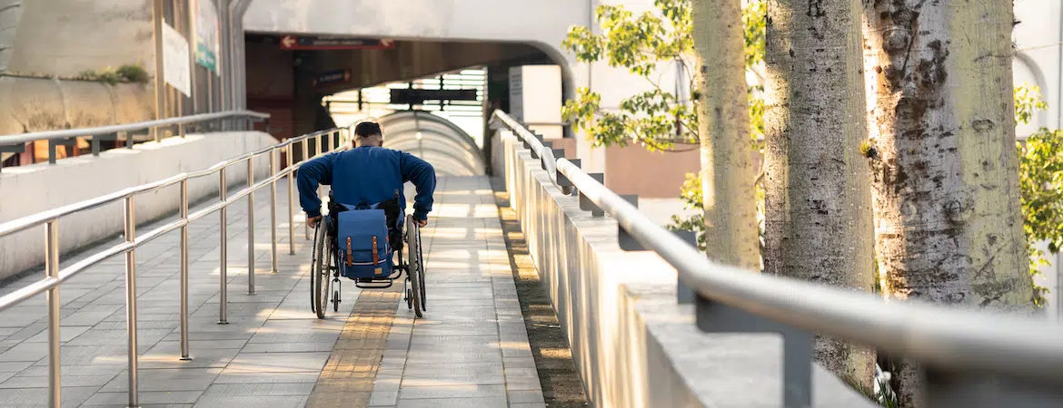 Un homme en fauteuil roulant entre dans une gare par une rampe d’accès PMR.
