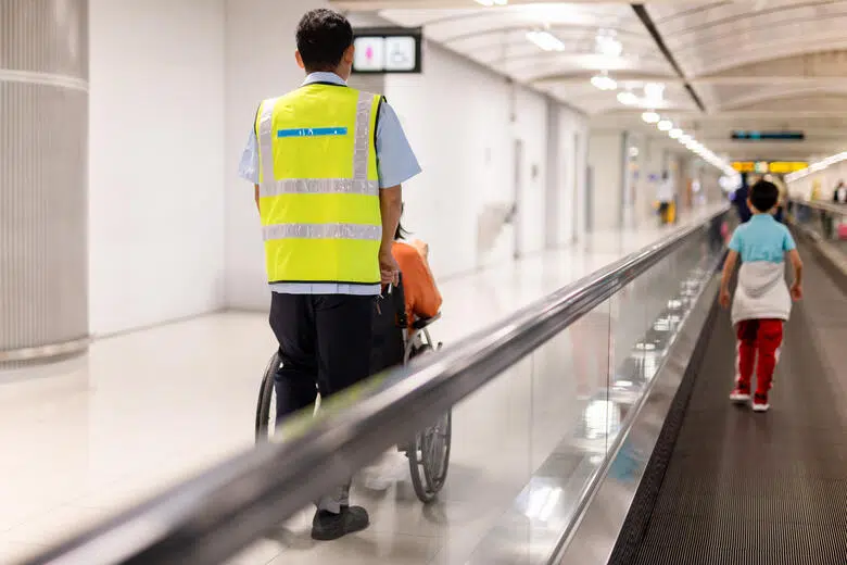 Une femme en fauteuil est assistée à un terminal d’aéroport.