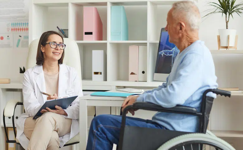 Un homme en fauteuil en consultation médicale avant son voyage avec un handicap.